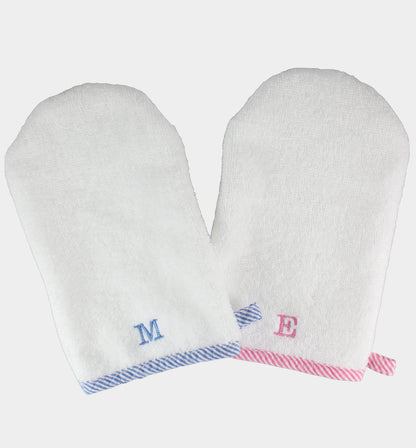 A pair of white bath mitts with blue and pink striped trim, featuring a monogrammed initial on the wrist area.